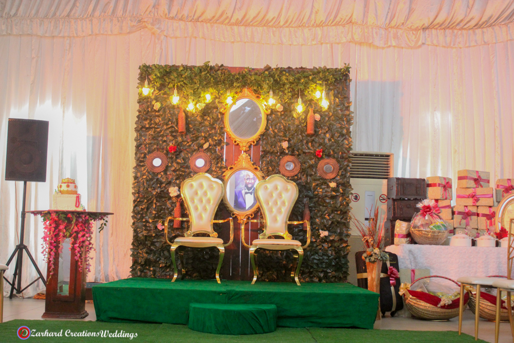 Traditional Wedding, eru iyawo set up for traditional engagement, yam n rack, boxes, baskets, palm oil, gift items for yoruba traditional wedding, parents sofa and couple chairs with green backdrop stage and mirrors with astroturf