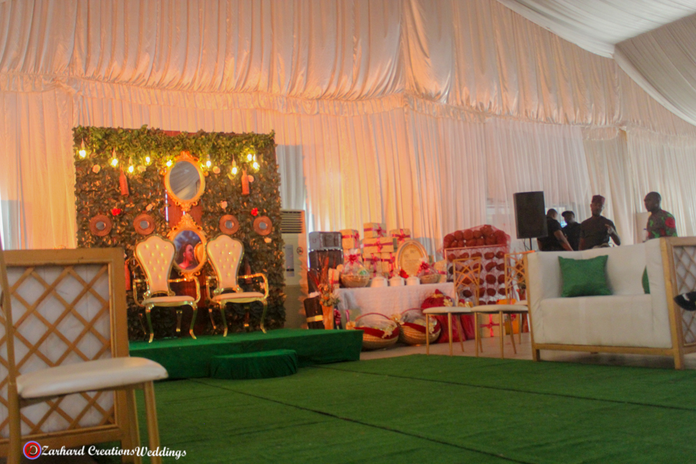 Traditional Wedding, eru iyawo set up for traditional engagement, yam n rack, boxes, baskets, palm oil, gift items for yoruba traditional wedding, parents sofa and couple chairs with green backdrop stage and mirrors with astroturf