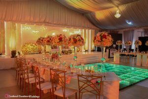 event wedding stage design, signage, chandelier, led dance floor, gold back chameleon chairs, curved VIP table with centerpieces, candles, charger plates, menu card, napkins, event decorator in Nigeria