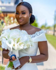 Bride wedding day dress, portrait photography outdoor, Debola and Okiki white wedding in Canada, white wedding dress gown, white suit on groom with black pant, buttonnaire, white floral bouquet with memorabilia picture of mum, elegant smile, bridal make up, wrist watch