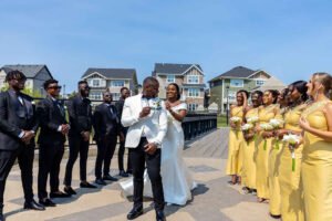 Nigerian white wedding in Canada, couple with friends picture, seamless wedding planning, white wedding dress gown, white suit on groom with black pant, buttonnaire, white floral bouquet with memorabilia picture of mum, elegant smile, bridal make up, wrist watch, couple with bridal party picture, photoshoot