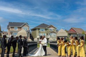 Outdoor wedding day photoshoot with kissing, bridesmaids and groomsmen, Debola and Okiki white wedding in Canada, white wedding dress gown, white suit on groom with black pant, buttonnaire,elegant smile, bridal make up, wrist watch