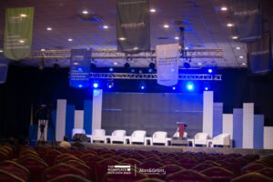 The WorkPlace Outlook conference planning in lagos, white bucket chairs with stools, panel session, screen, corporate event stage set up, ceiling installation with flags, banquet chairs