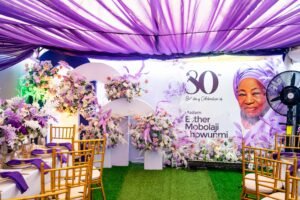 purple and white birthday design for 80th year old grandma with chiavari chairs, green astroturf, flowers, purple table scape, table setting, gold rim plates, purple floral arrangement on tables