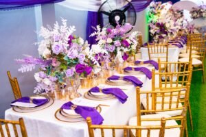 purple and white birthday design for 80th year old grandma with chiavari chairs, green astroturf, flowers, purple table scape, table setting, gold rim plates, purple floral arrangement on tables