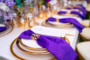 purple and white birthday design for 80th year old grandma with chiavari chairs, green astroturf, flowers, purple table scape, table setting, gold rim plates, purple floral arrangement on tables, menu card