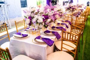 purple and white birthday design for 80th year old grandma with chiavari chairs, green astroturf, flowers, purple table scape, table setting, gold rim plates, purple floral arrangement on tables
